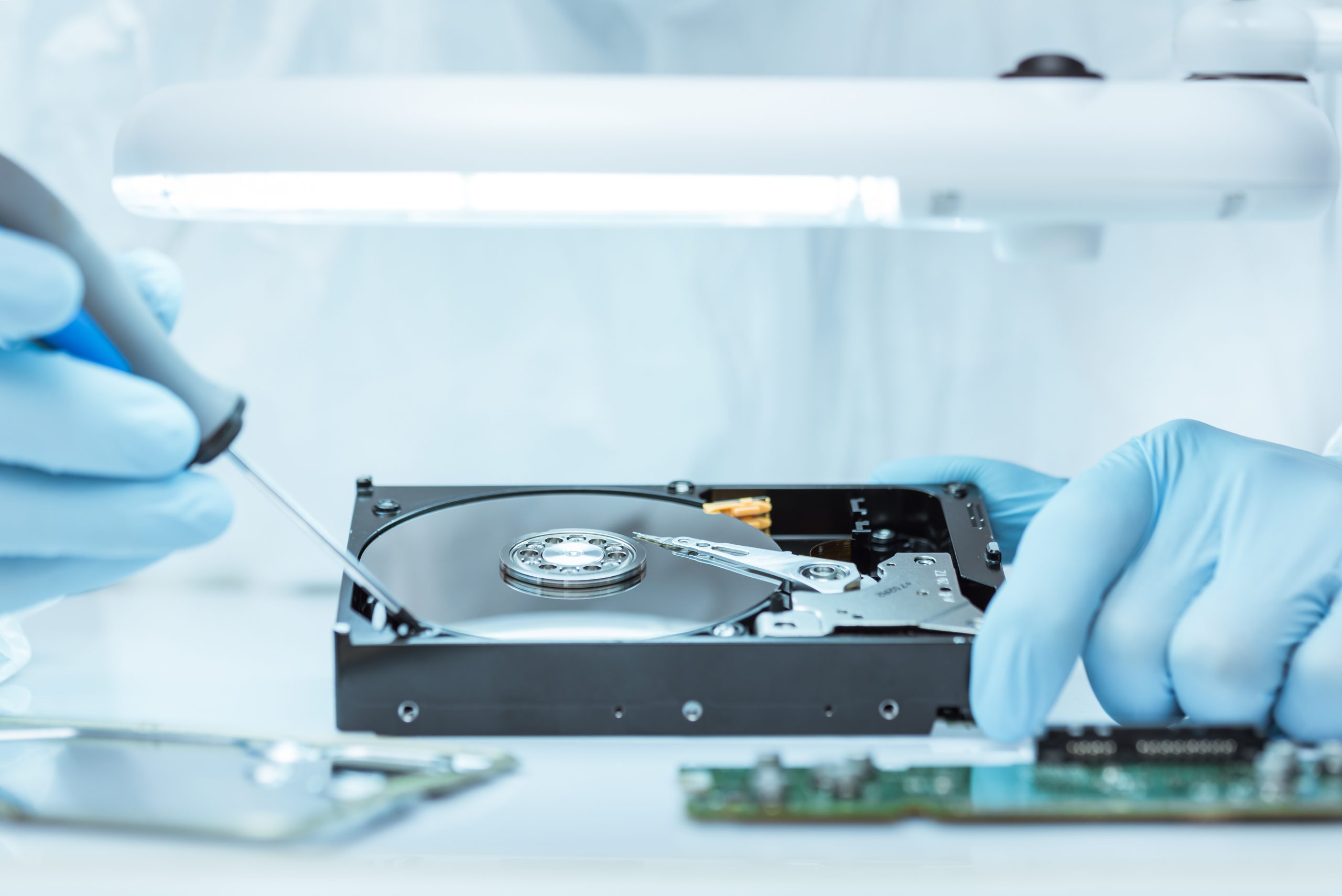 Hard Drive Repair and Data Recovery in Progress A technician wearing blue gloves carefully works on an open hard drive under a bright light, performing intricate data recovery or hardware repair.