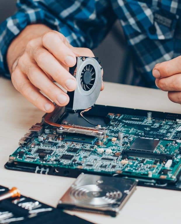Technician replacing a cooling fan on a laptop motherboard using specialized tools.