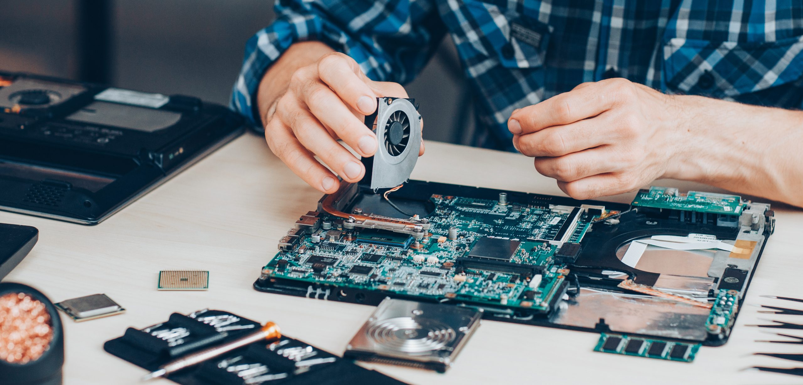 Expert Laptop Cooling Fan Replacement Service Technician replacing a cooling fan on a laptop motherboard using specialized tools.