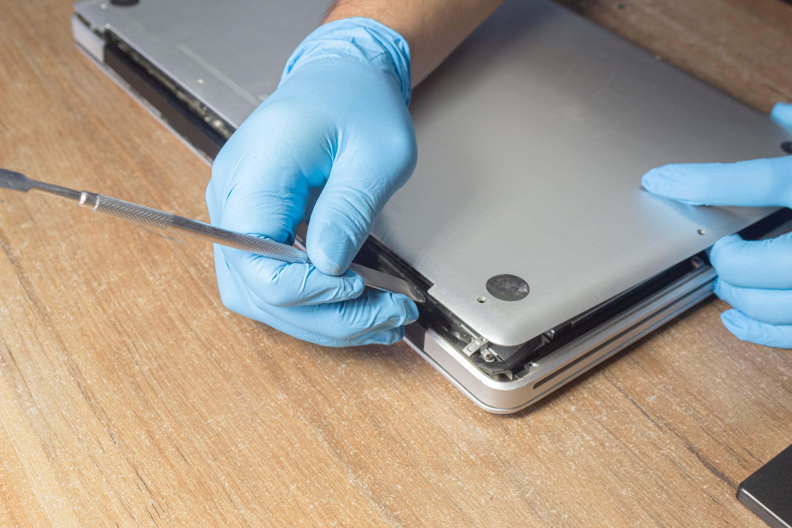 Laptop Repair and Maintenance Technician wearing gloves repairing a laptop with precision tools on a wooden surface.