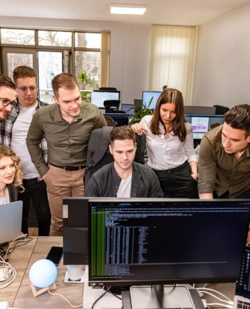 Professional Team Collaboration in Modern Office A team of professionals collaborating in a modern office environment, gathered around a computer screen, discussing technical solutions.