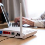 Professional Wi-Fi Router Setup and IT Support Close-up of a Wi-Fi router with a laptop user in the background, representing IT support for home and office network setups.