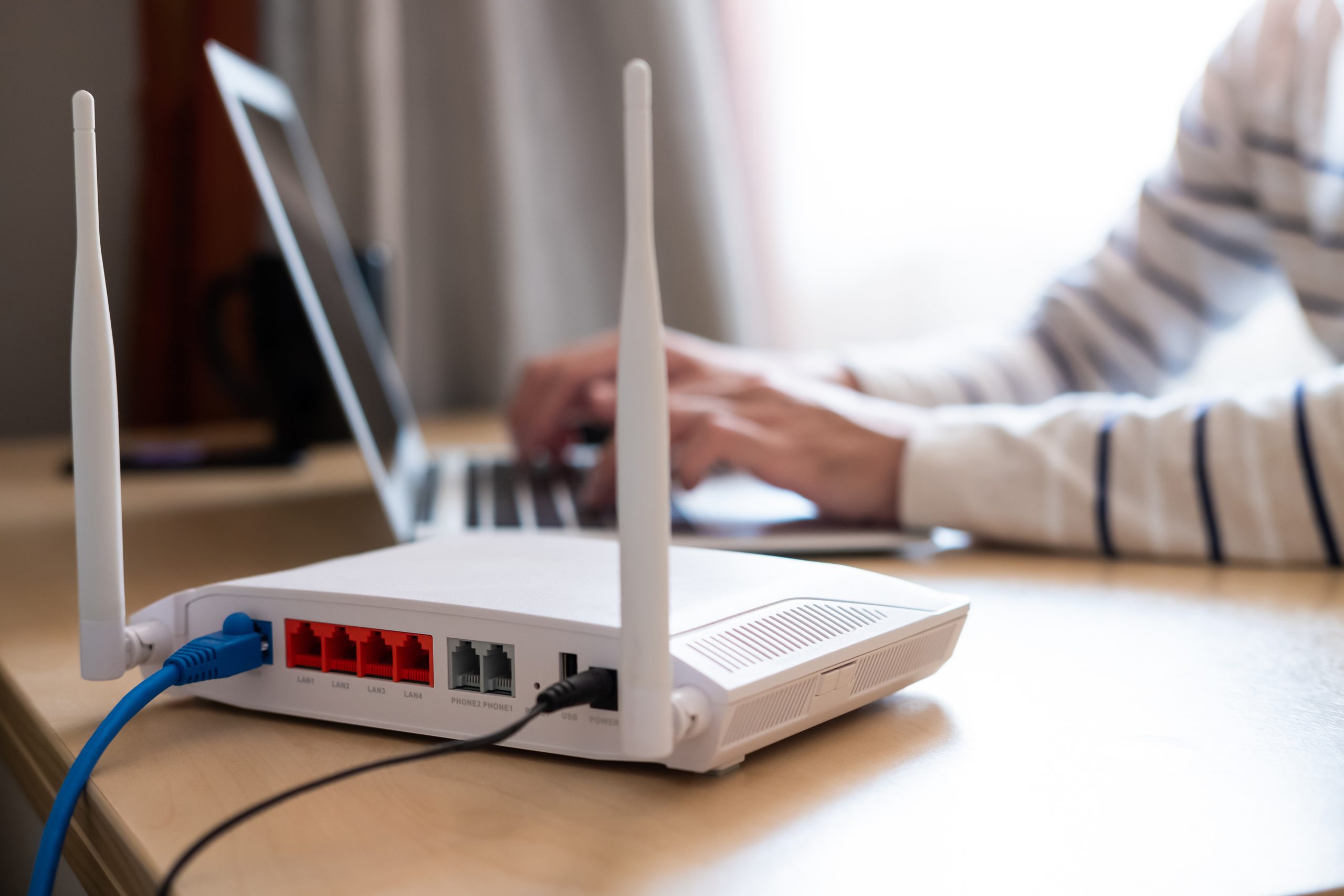 Professional Wi-Fi Router Setup and IT Support Close-up of a Wi-Fi router with a laptop user in the background, representing IT support for home and office network setups.