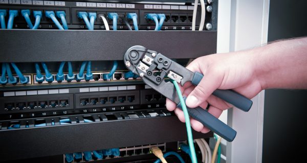 Cable Crimping Tool in Use During Network Installation A hand using a cable crimping tool to secure a green network cable in a patch panel with blue cables.