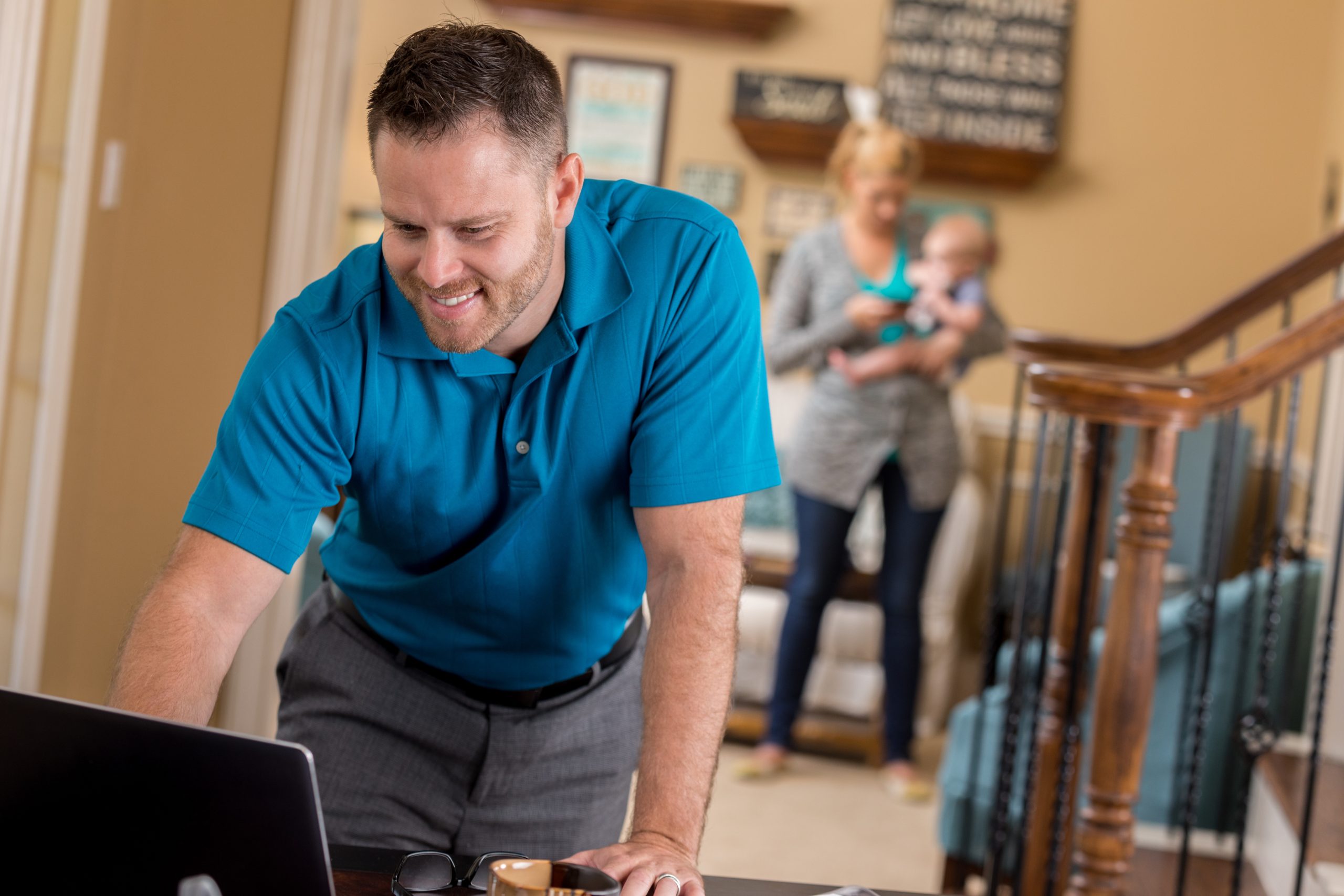 Home IT Support Services in Aurora | IT Tech LLC A smiling man working on a laptop at home, with a family in the background, representing home IT support services.