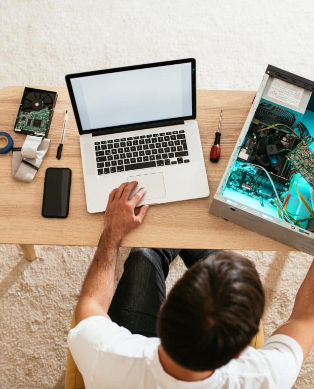 "A person working on data transfer between a laptop and a desktop computer, surrounded by tools and components.