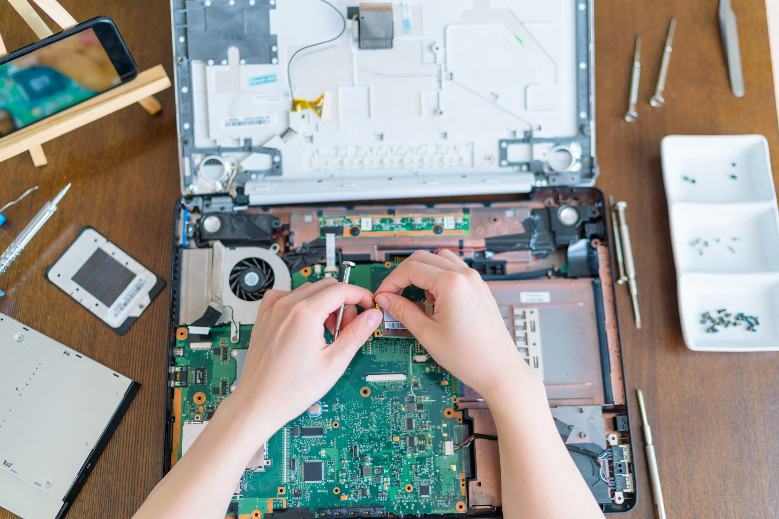 Laptop Motherboard Repair in Progress Technician repairing a laptop motherboard with precision tools on a wooden desk in Denver.