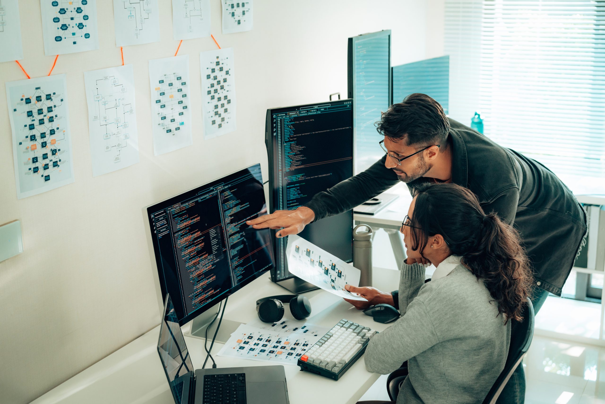 Software Optimization & Upgrade Collaboration Two IT professionals analyzing software performance and discussing optimization strategies on a multi-monitor setup.